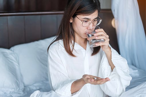 Woman in bed, drinking water and preparing to take a sleep supplement.