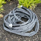 The Teknor Apex Zero-G Hose sits in a coil amidst some mulch.