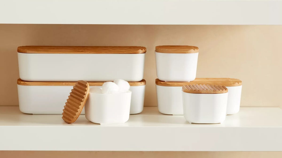 A set of white Squared Away storage bins with wooden lids on a white bathroom shelf.