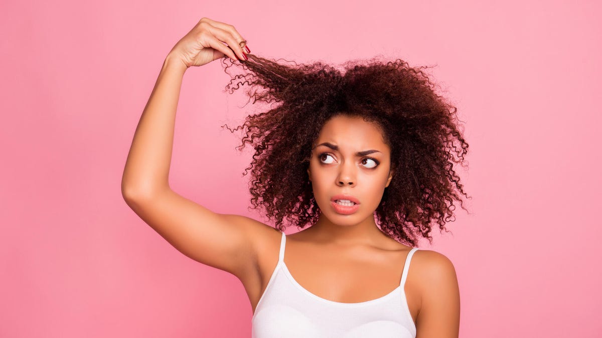 Woman holding a strand of hair in hand while looking displeased about hair health