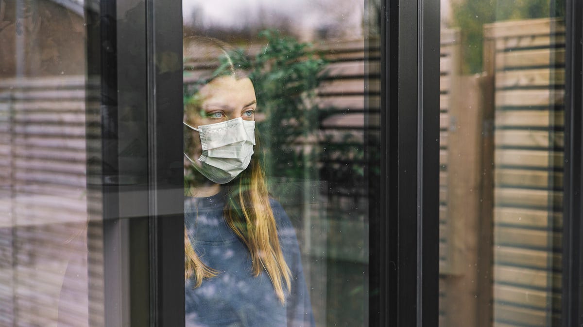 teenage girl looking through window with mask 