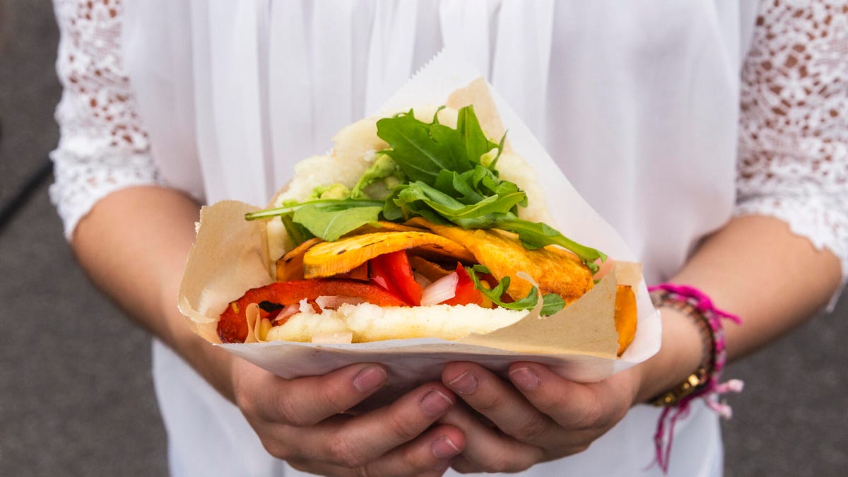 woman in white shirt holding vegan sandwich, close-up of hands