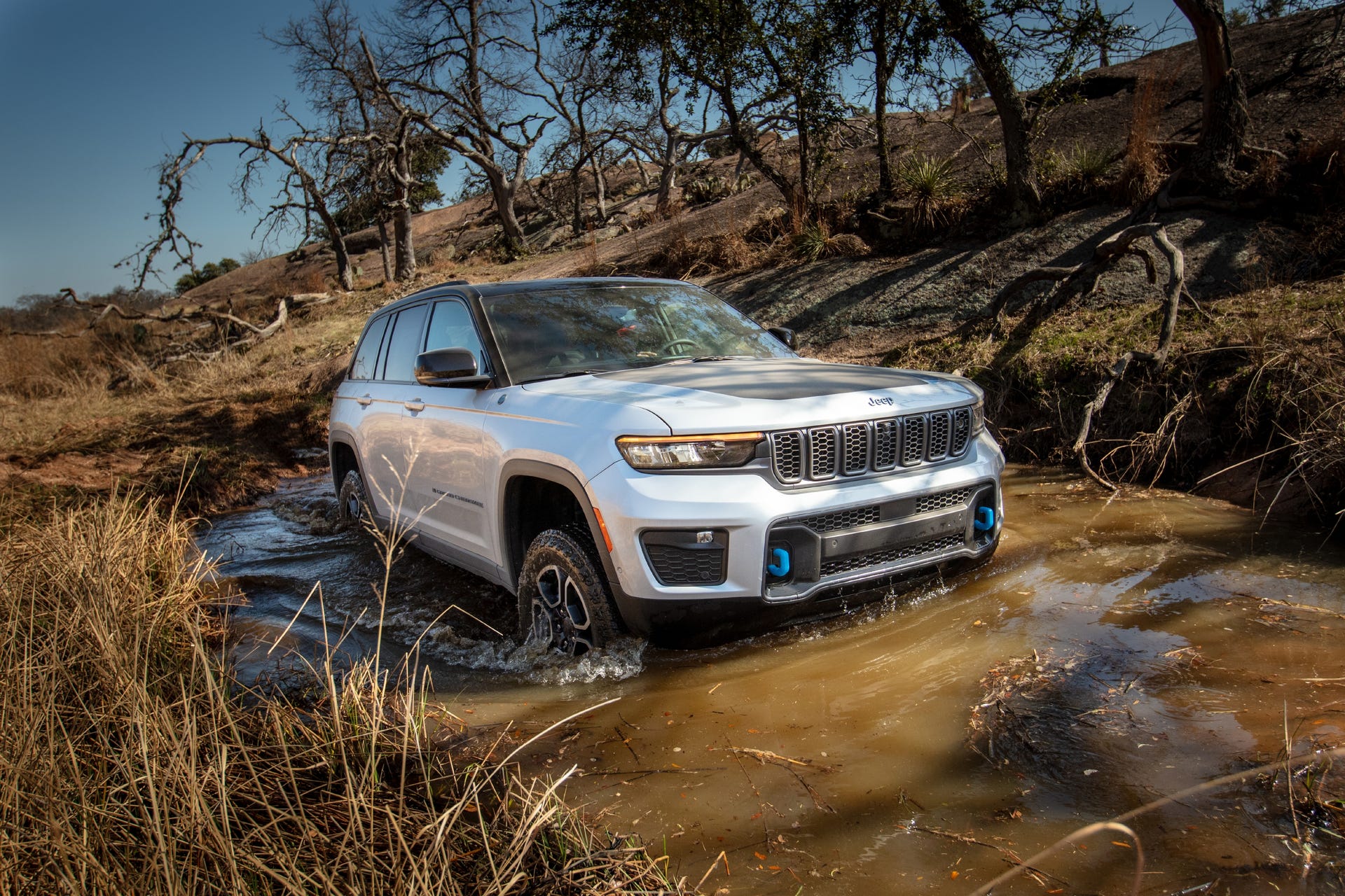 Front 3/4 view of a 2022 Jeep Grand Cherokee 4xe wading through muddy water