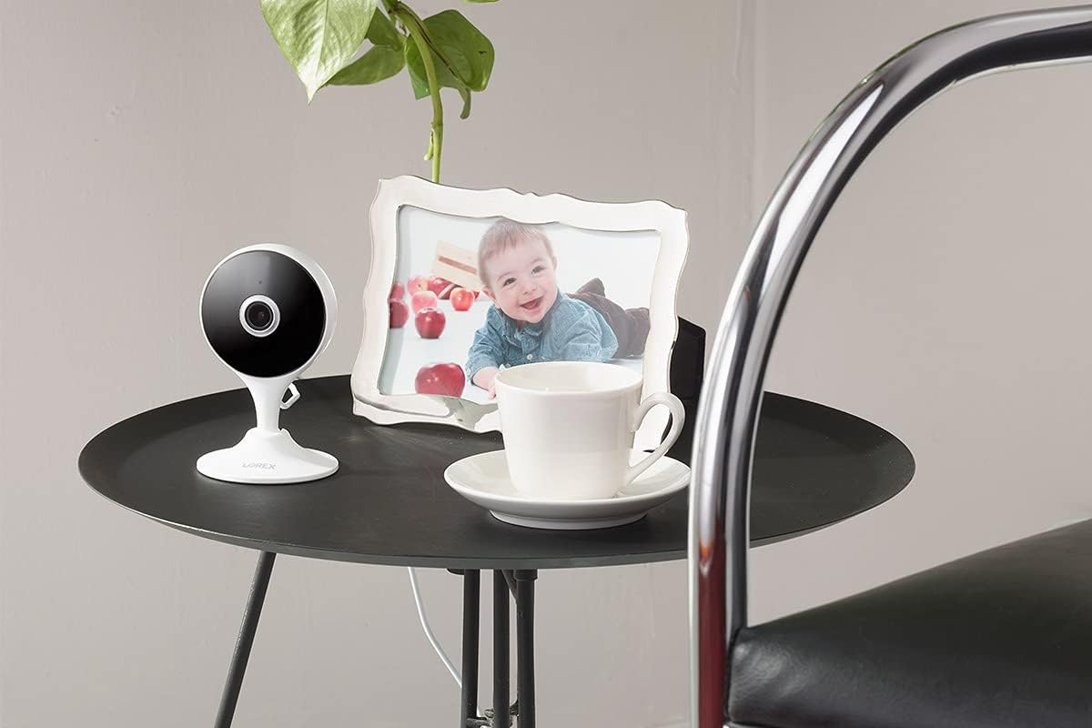 The Lorex indoor security camera sitting on a small black table with a cup and saucer and a child's photo.