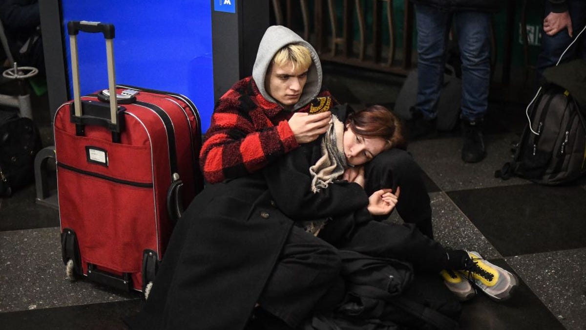 A man checks a smartphone for information while taking shelter in a metro station in Kyiv, Ukraine, on Thursday. A tired-looking woman rests her head on his knee.