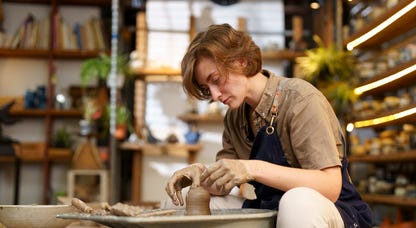 Woman sitting in front of a pottery wheel, molding clay.