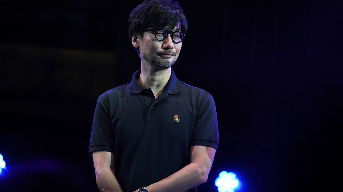 hideo kojima standing looking to his left wearing a blue polo shirt