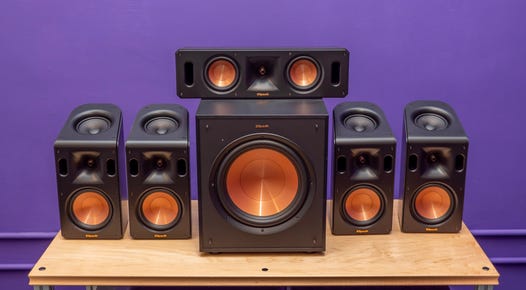 Klipsch Reference Cinema System 5.1.4 With Dolby Atmos surround sound speakers on a wood table with a purple background.