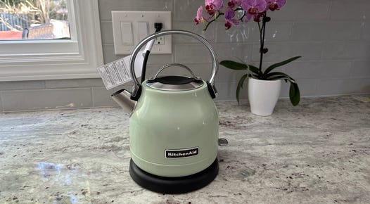 A pistachio green-colored KitchenAid KEK1222 electric kettle sits on a granite countertop.