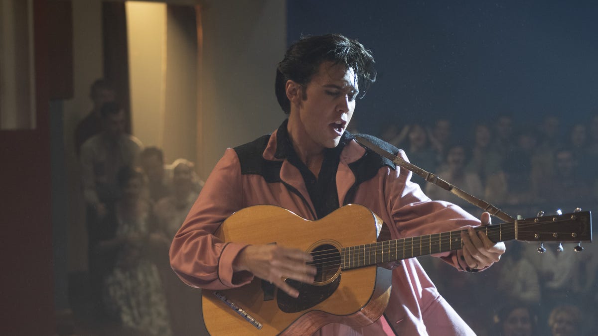 Austin Butler as Elvis Presley, in a pink suit holding a guitar.