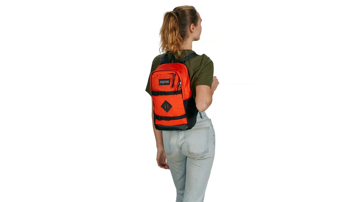 A girl wearing jeans and a green shirt faces away while wearing an orange JanSport Off Campus Sling bag.