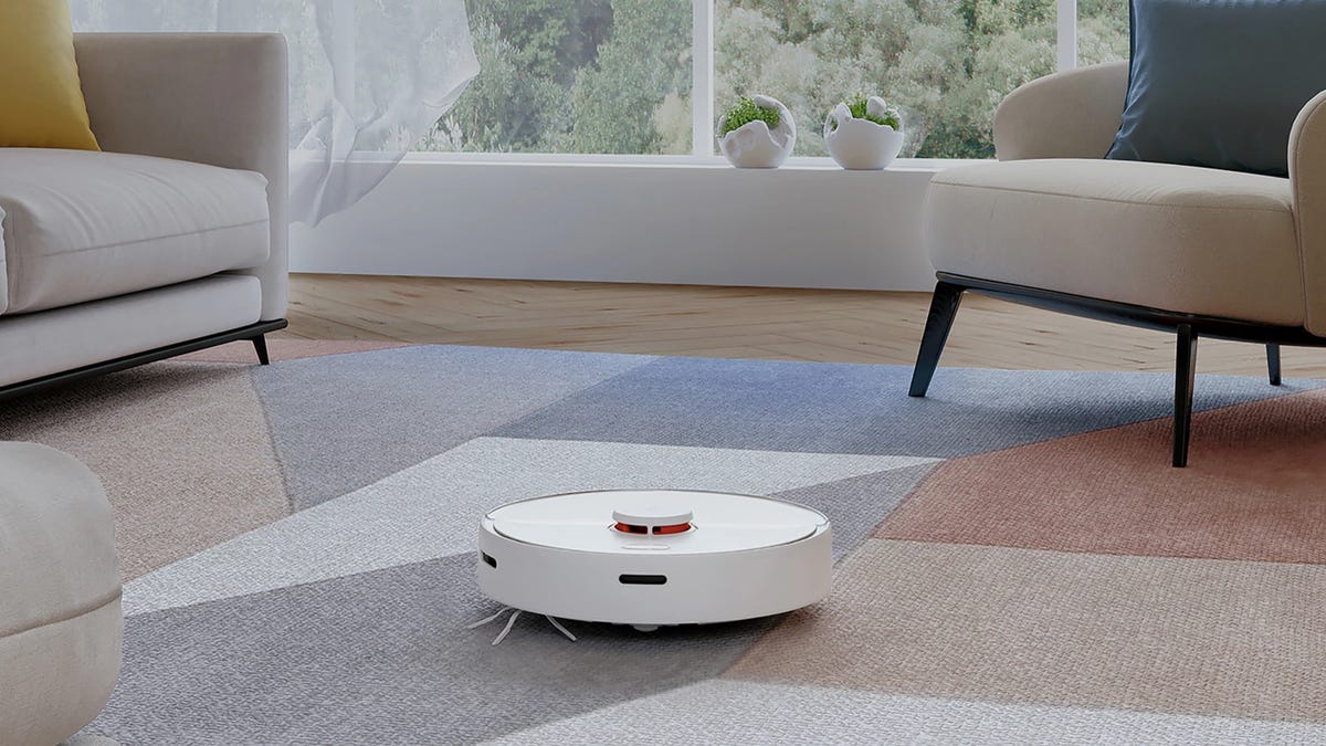 A white Roborock S6 Pure robot vacuum cleaning a living room carpet.