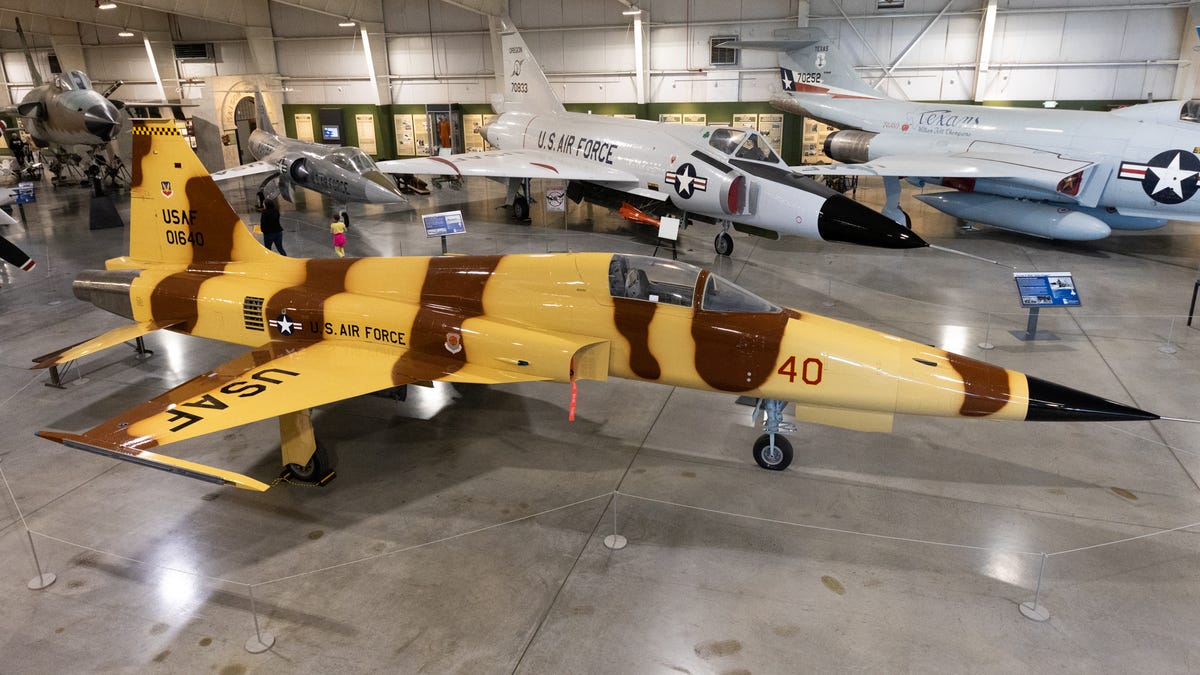 Looking down and at an angle on a sleek F-5 fighter aircraft painted in yellow and brown stripes.