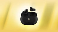 A pair of black Beats Studio Buds Plus earbuds against a yellow background.