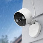 An illustration of the Tapo C120 camera mounted to white siding outside in the rain.