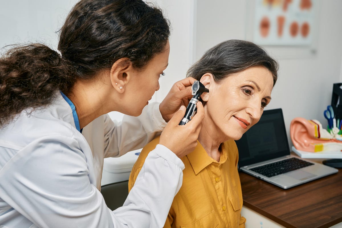 Médico otorrinolaringólogo revisando el oído de una mujer madura usando un otoscopio.