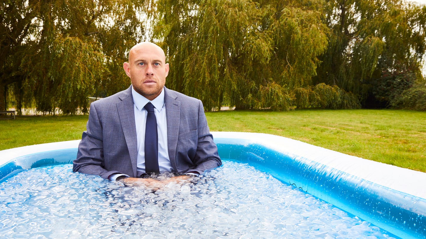 A man wearing a suit, in an inflatable pool filled with ice and water