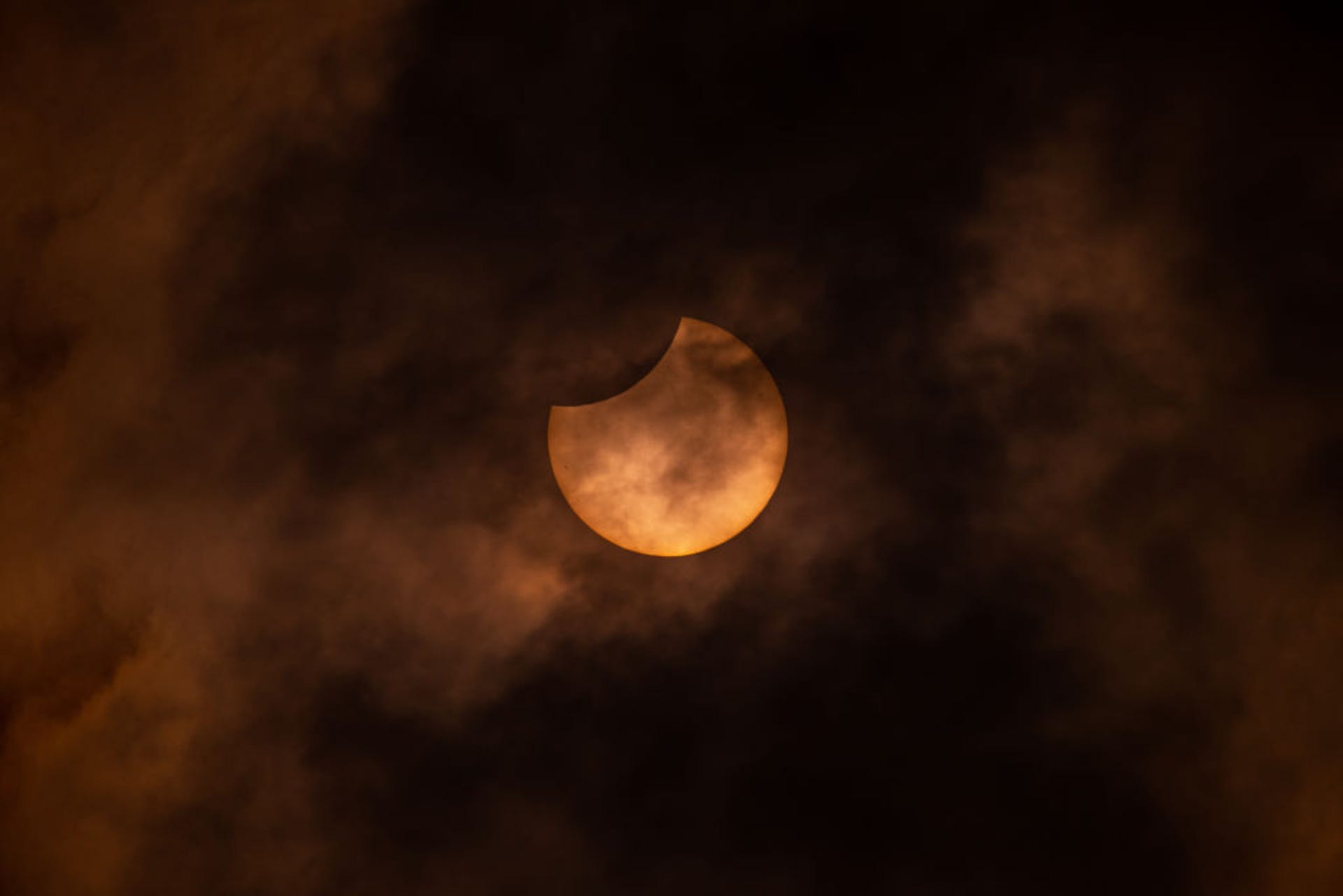 The glowing solar eclipse seen through the murky clouds in Italy