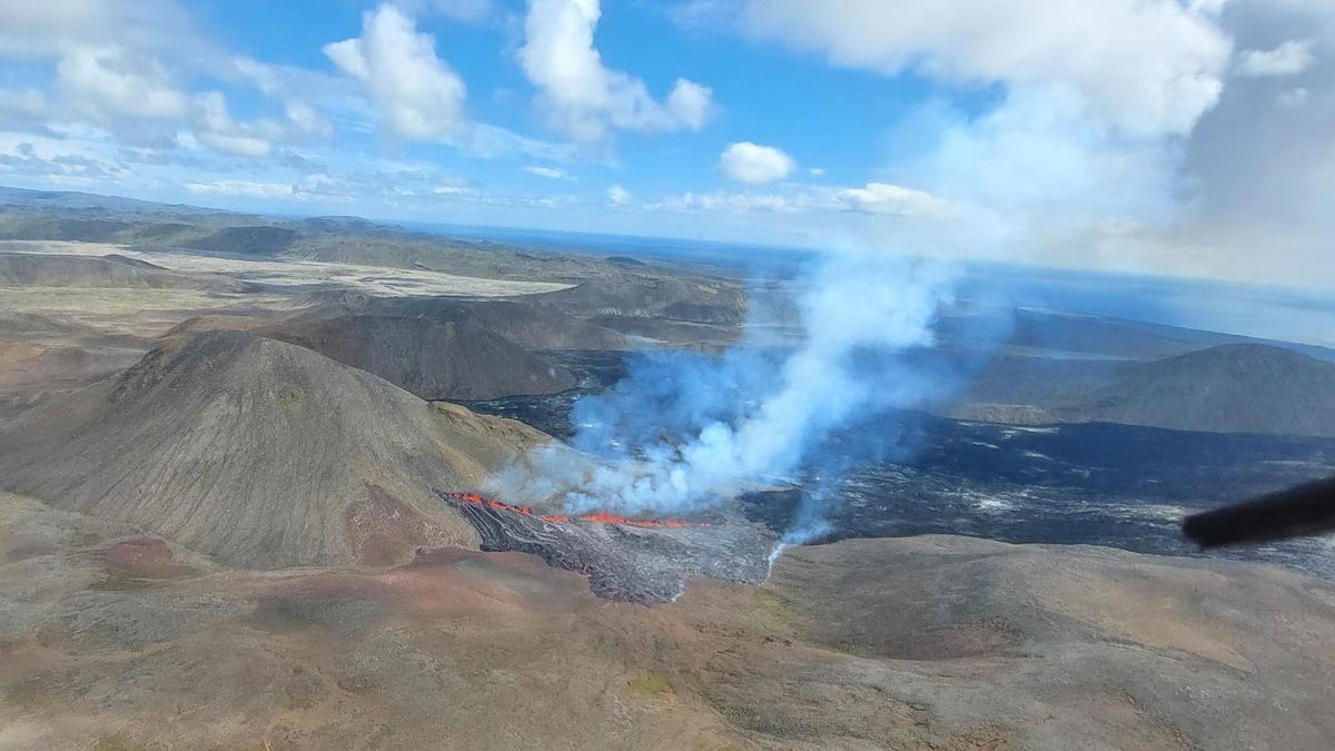 A bright red volcanic fissure spits out a cloud from the rugged brown Icelandic landscape.