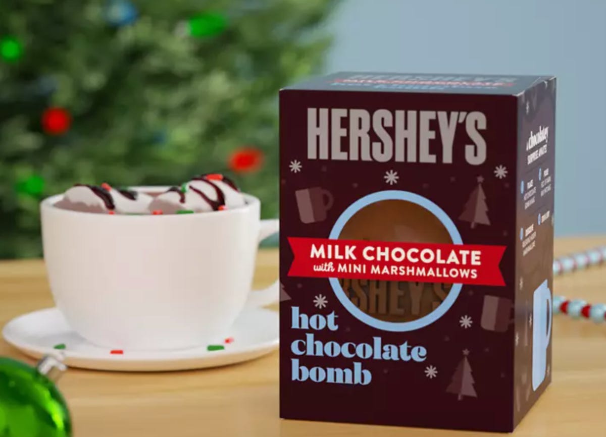 a hot chocolate bomb beside a white mug filled with hot chocolate.