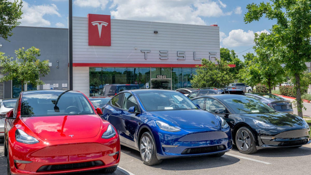 Three Tesla Model Y EVs sitting in a Tesla dealership parking lot.