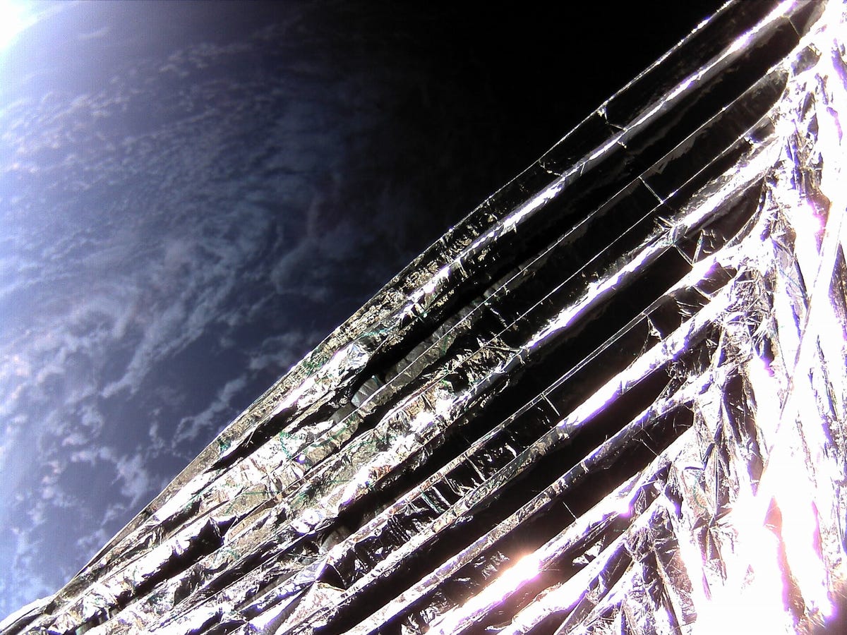 La Tierra se ve a lo lejos desde la perspectiva del satélite ION.  Cubrir la mayor parte de la pantalla es parte de la vela espacial de ruptura.