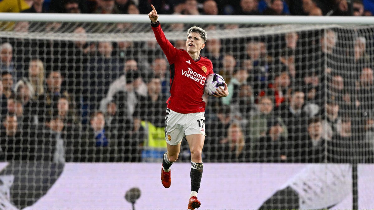 Alejandro Garnacho of Manchester United celebrating, pointing upwards with his right hand outstretched, with a ball under his left arm, running with the goal behind him.