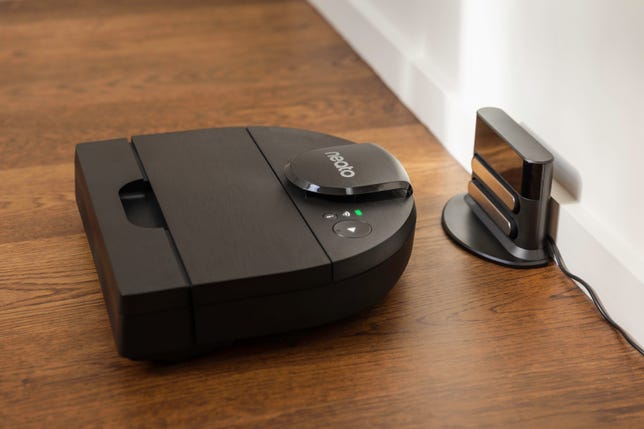 The D-shaped Neato D9 robot vacuum backs into its charging dock.