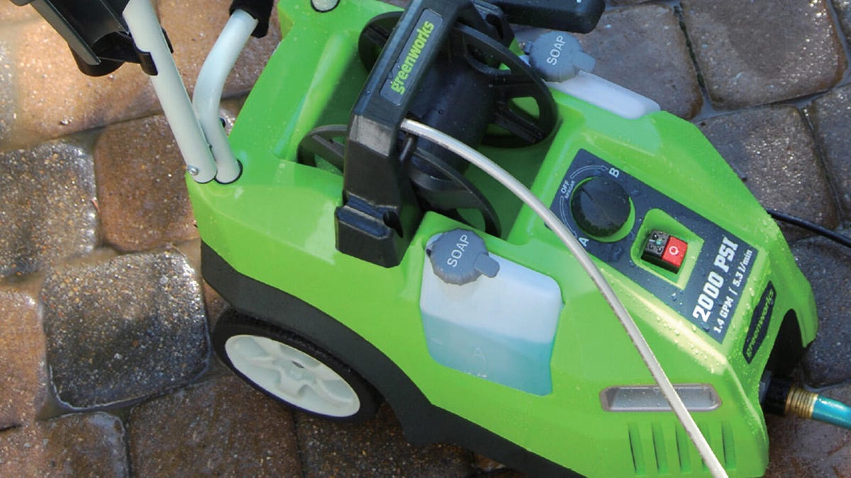 The 2000 PSI corded electric pressure washer by Greenworks rests on top of wet pavers.