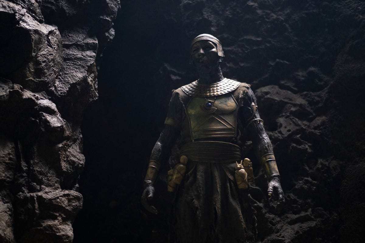 A masked Heka priest stands in a shadowy cave in Moon Knight episode 4.
