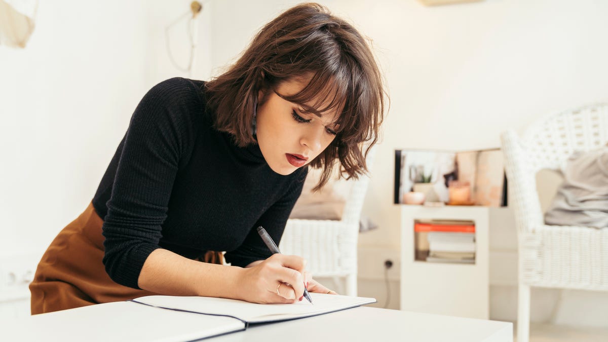 A woman is standing at a desk and writing on a piece of paper.
