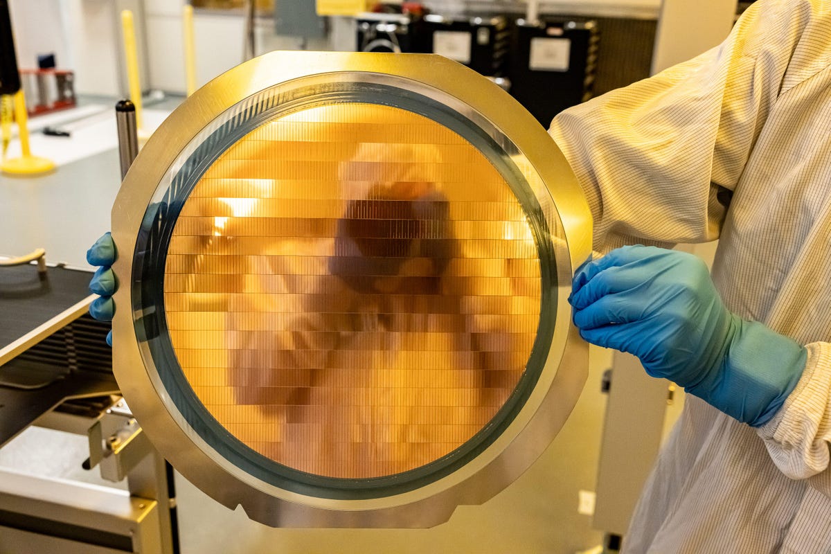 CNET reporter Stephen Shankland is reflected in a 300mm silicon wafer tiled with hundreds of slivers of silicon, each a tiny bridge to be tucked under adjoining processor chiplets to serve as a communications link. They're a key part of Intel's EMIB packaging technology.