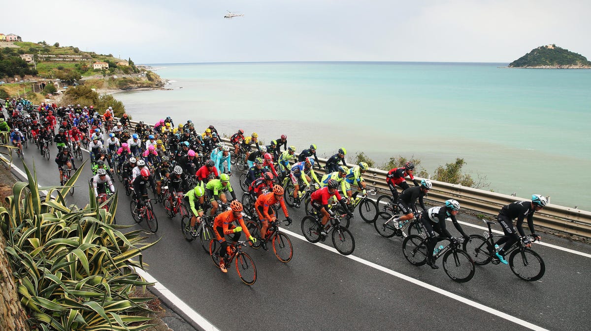 A large group of cyclists competing in the Milan-San Remo race, riding along a picturesque coastal road.