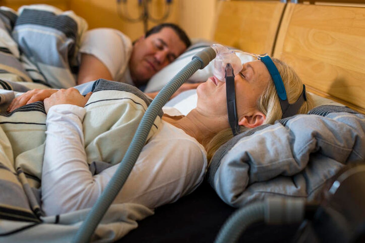 Woman sleeping with a sleep apnea mask next to her partner.