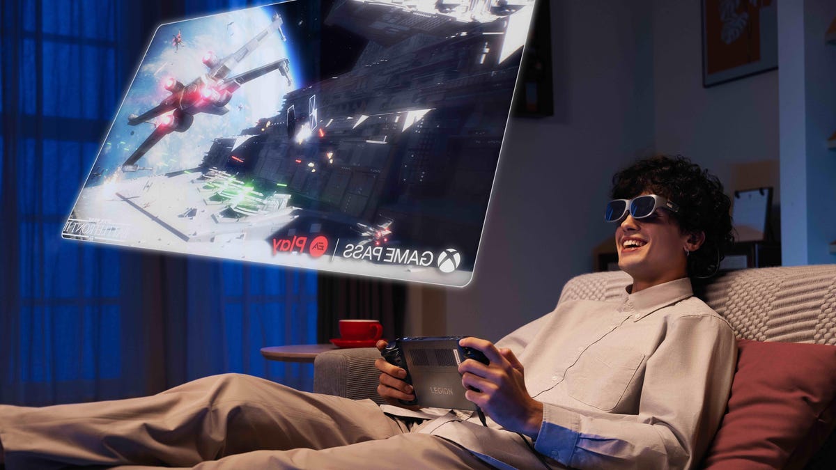 Man wearing glasses and playing a game on a display hovering over his sofa