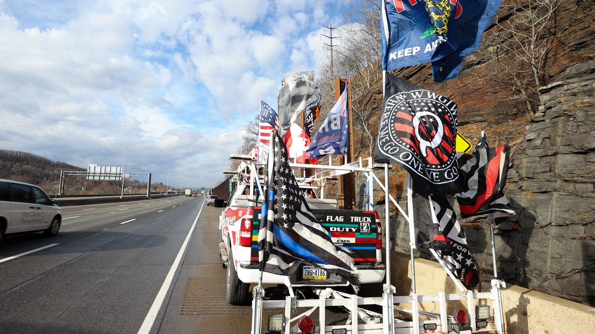 a truck with a trailer filled with multiple flags supporting donald trump and qanon