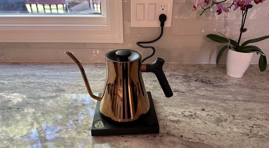 The Stagg EKG Electric Kettle in a polished copper finish sitting on a granite countertop.
