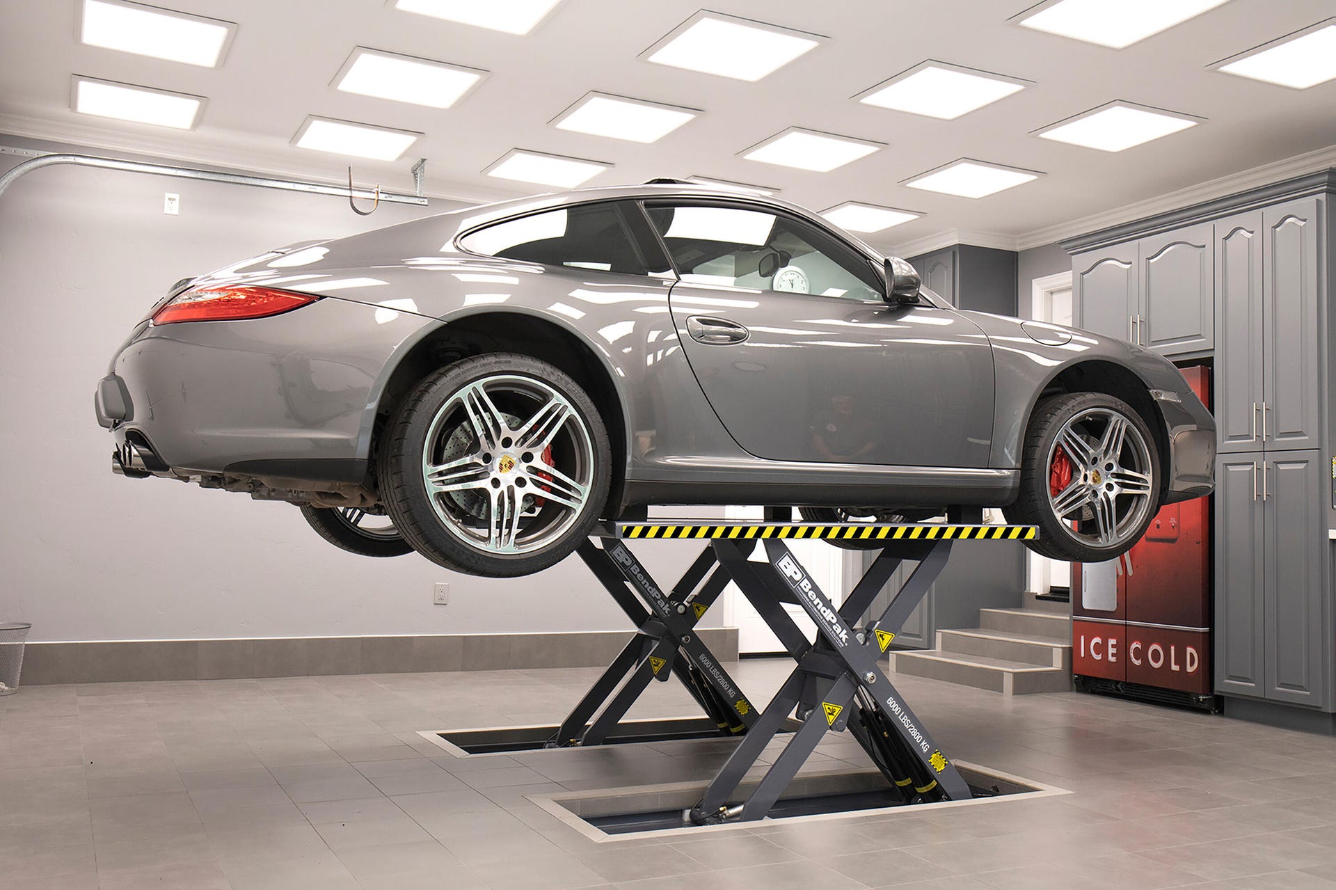 A gray car being held up by a BendPak scissor lift. 