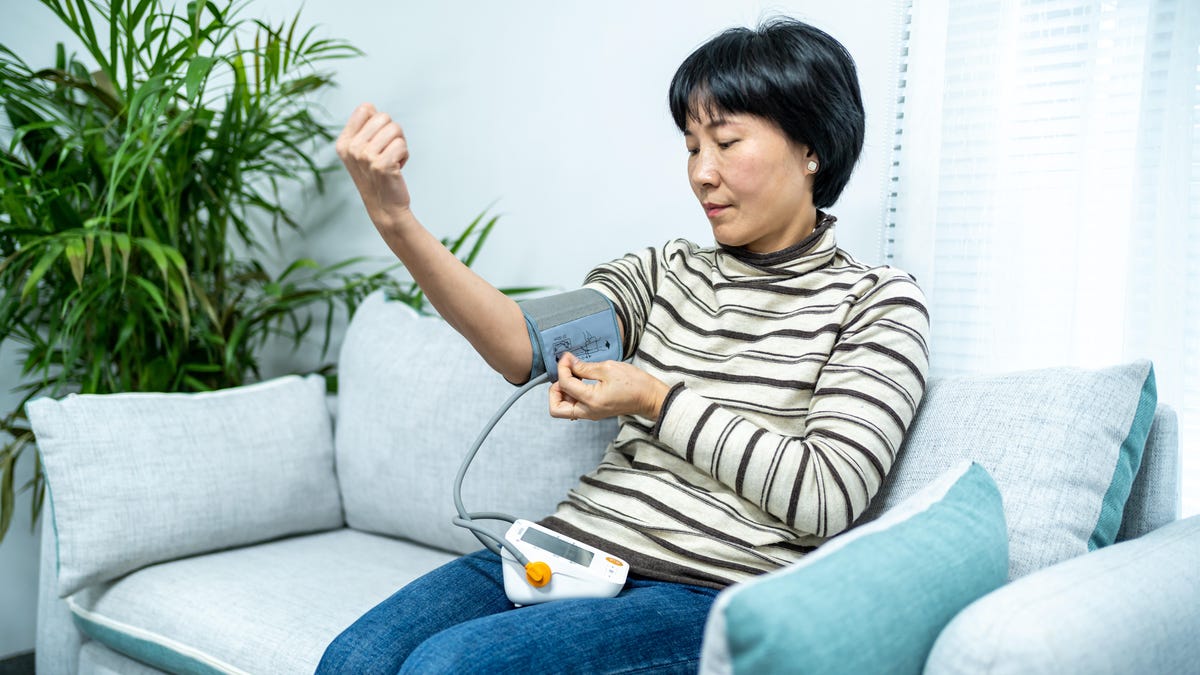 Woman sitting on couch takes her blood pressure.