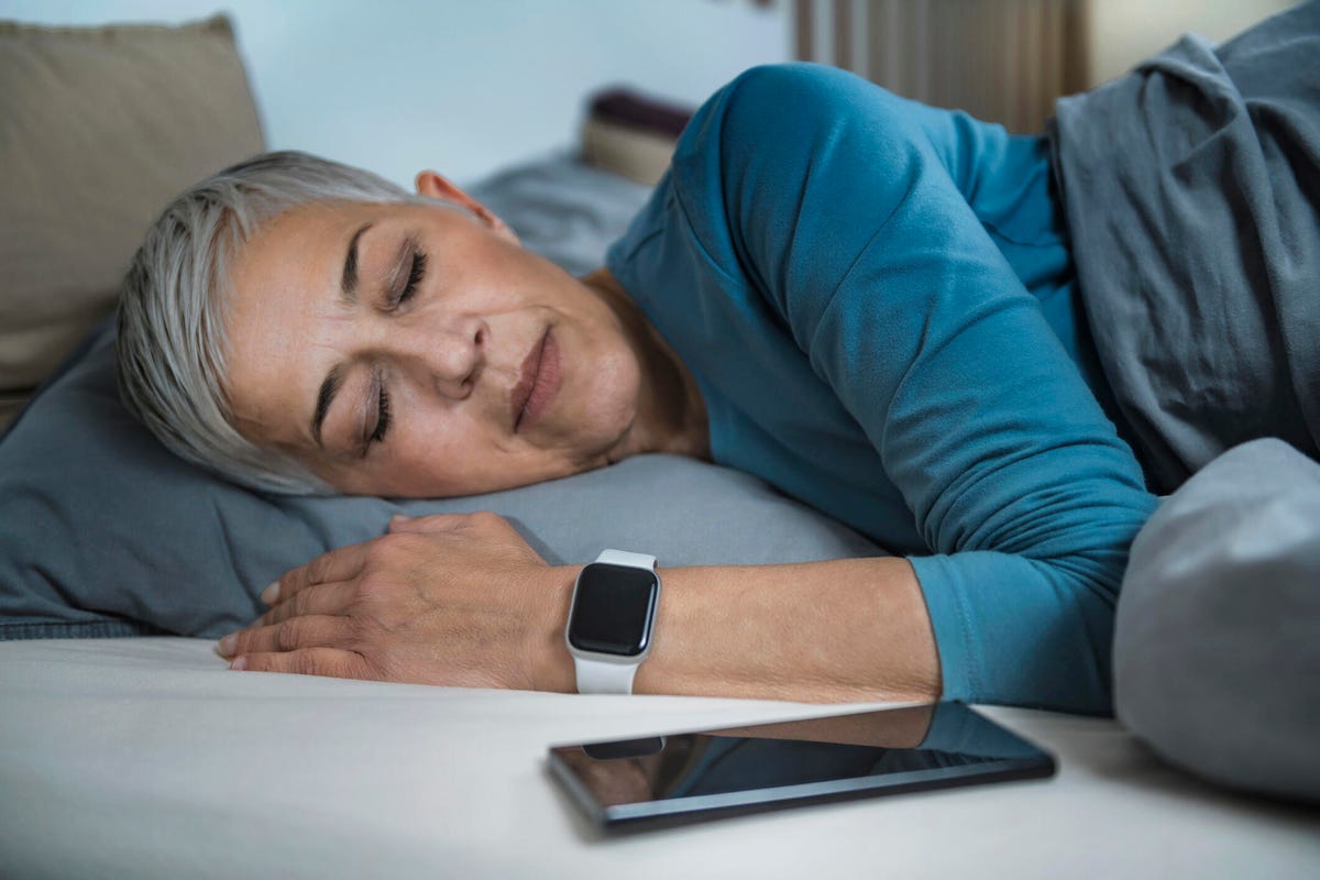 Woman sleeping with a sleep tracking watch and phone next to her on the bed