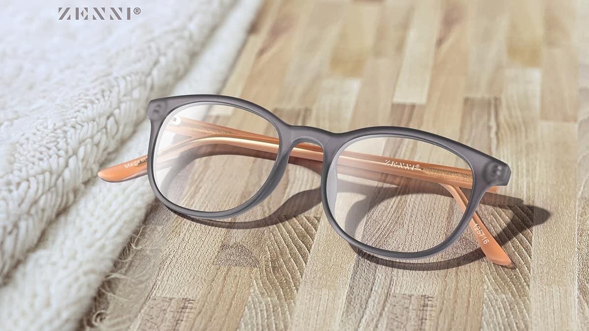 A pair of brown eyeglasses sit folded on a wooden floor next to a folded white carpet