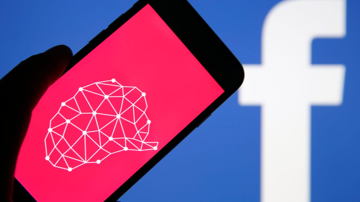 A phone shows a pink Cambridge Analytica logo in front of a large blue Facebook logo