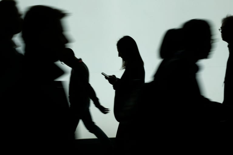 A woman looks at a smartphone as other people rush by.