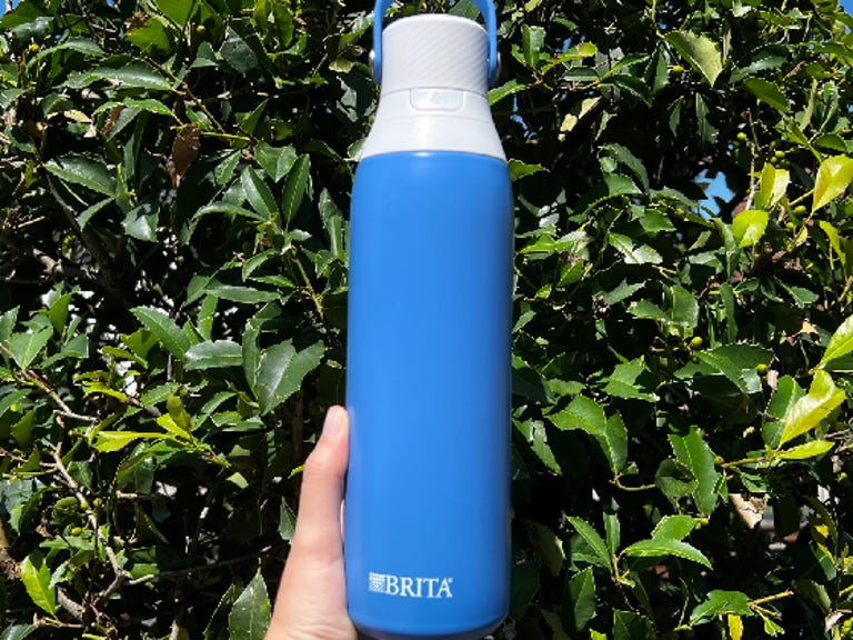 A hand holding Brita Stainless Steel Filtering Water Bottle in front of a tree.