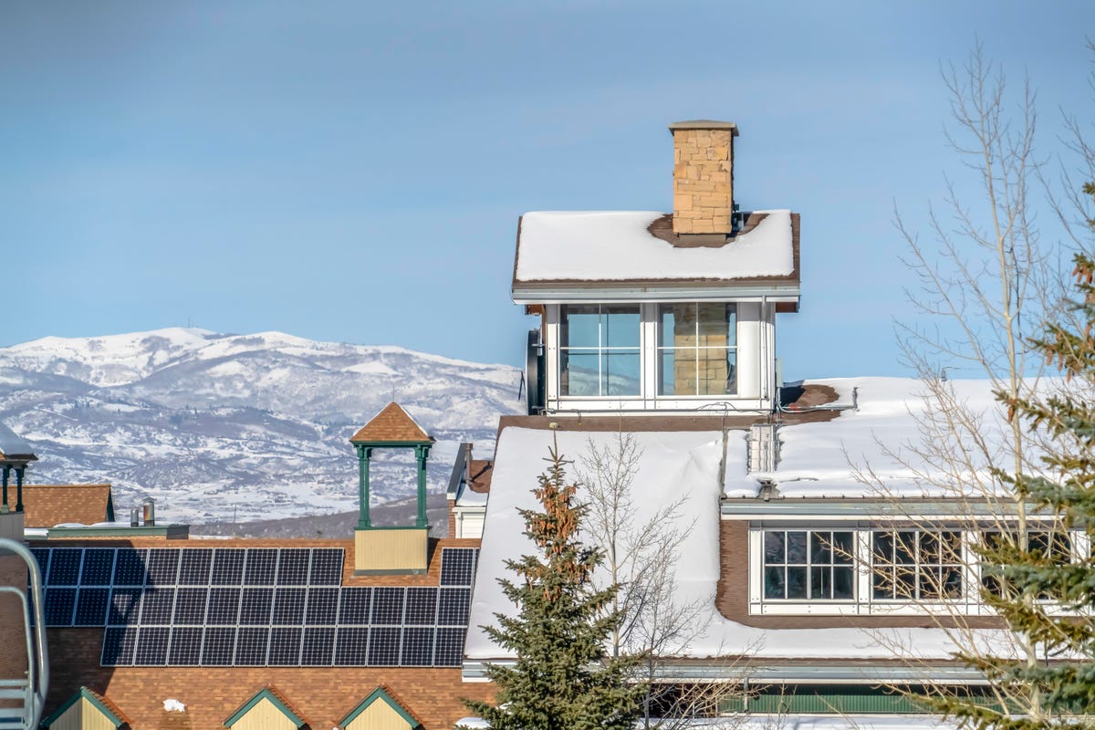 Solar panels on a snowy roof with mountains in the background.