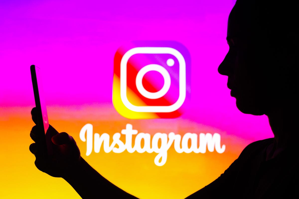 A woman's silhouette is holding a smartphone with an Instagram logo in the background