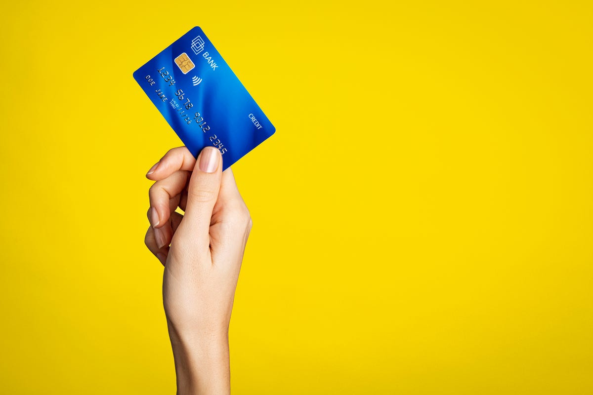 A hand holding up a credit card against a yellow background