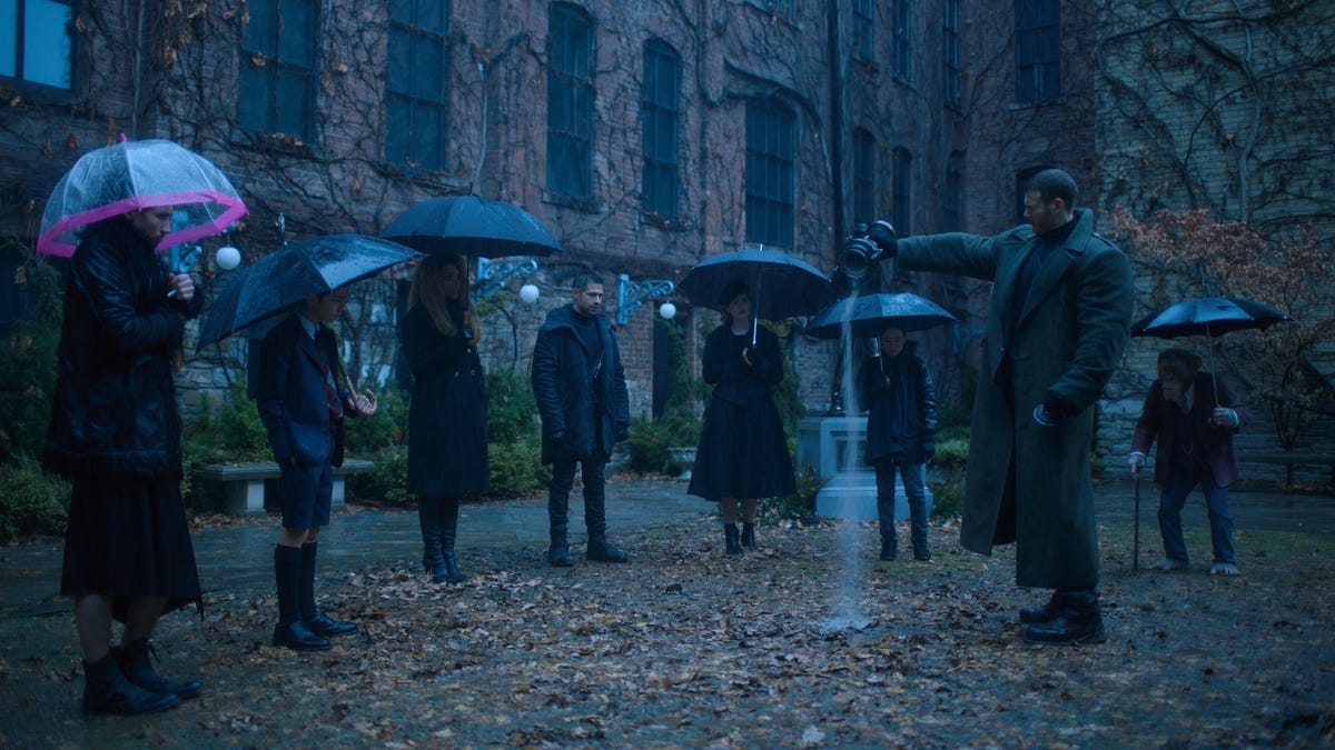 The characters of Umbrella Academy stand in a courtyard holding umbrellas