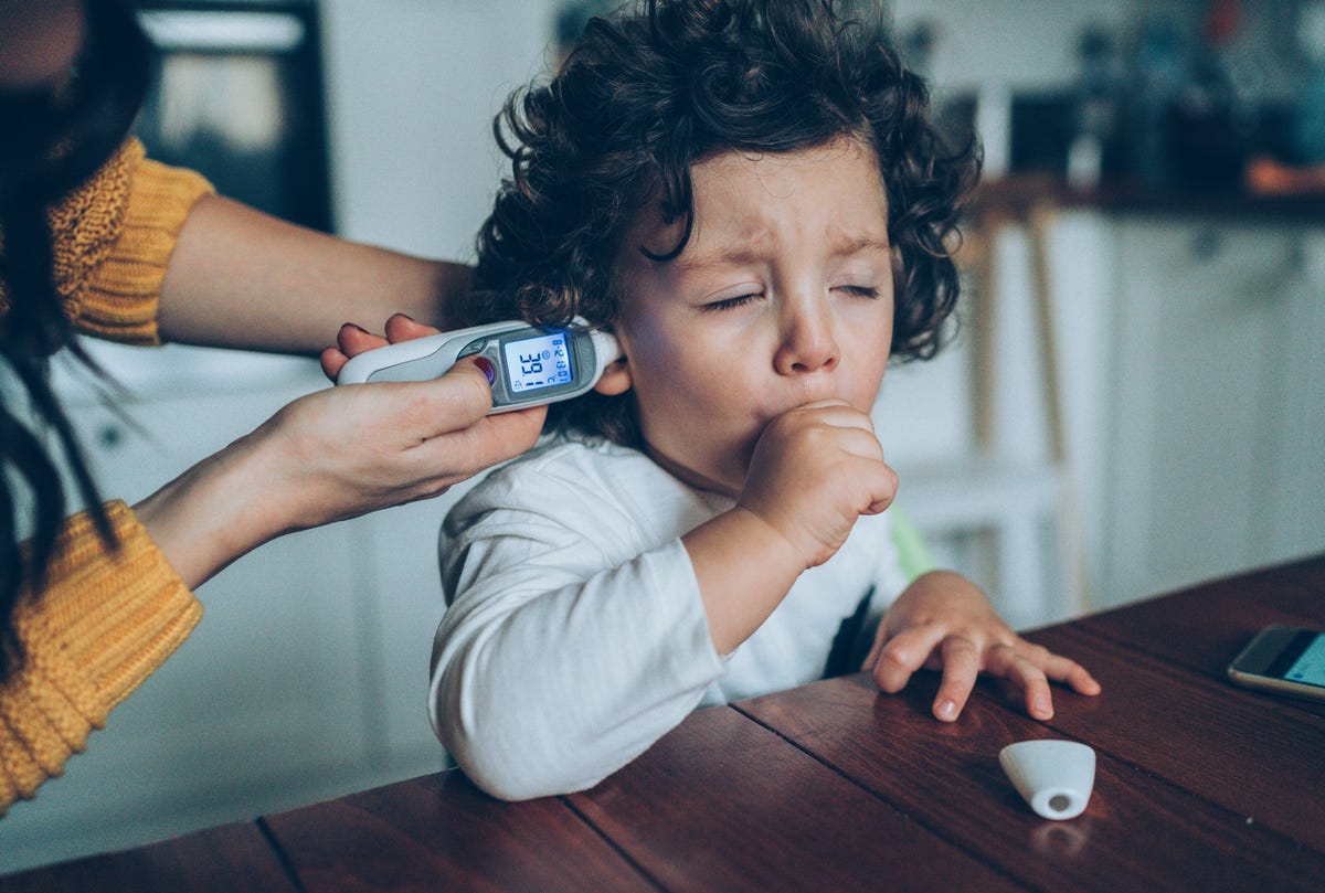 A three-year-old coughs while his mother takes his temperature