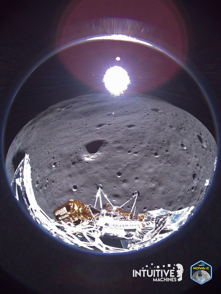 Fisheye image showing, at the bottom, part of the lander; in the middle, the lunar surface with its distinctive craters; and up top, a bright white circle against the darkness of space, with a small bright crescent to its left.